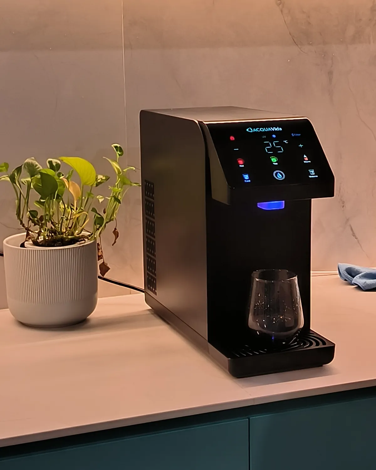 The LUNA on a marble kitchen counter under the cabinet lights, a glass on its tray and a potted plant beside it