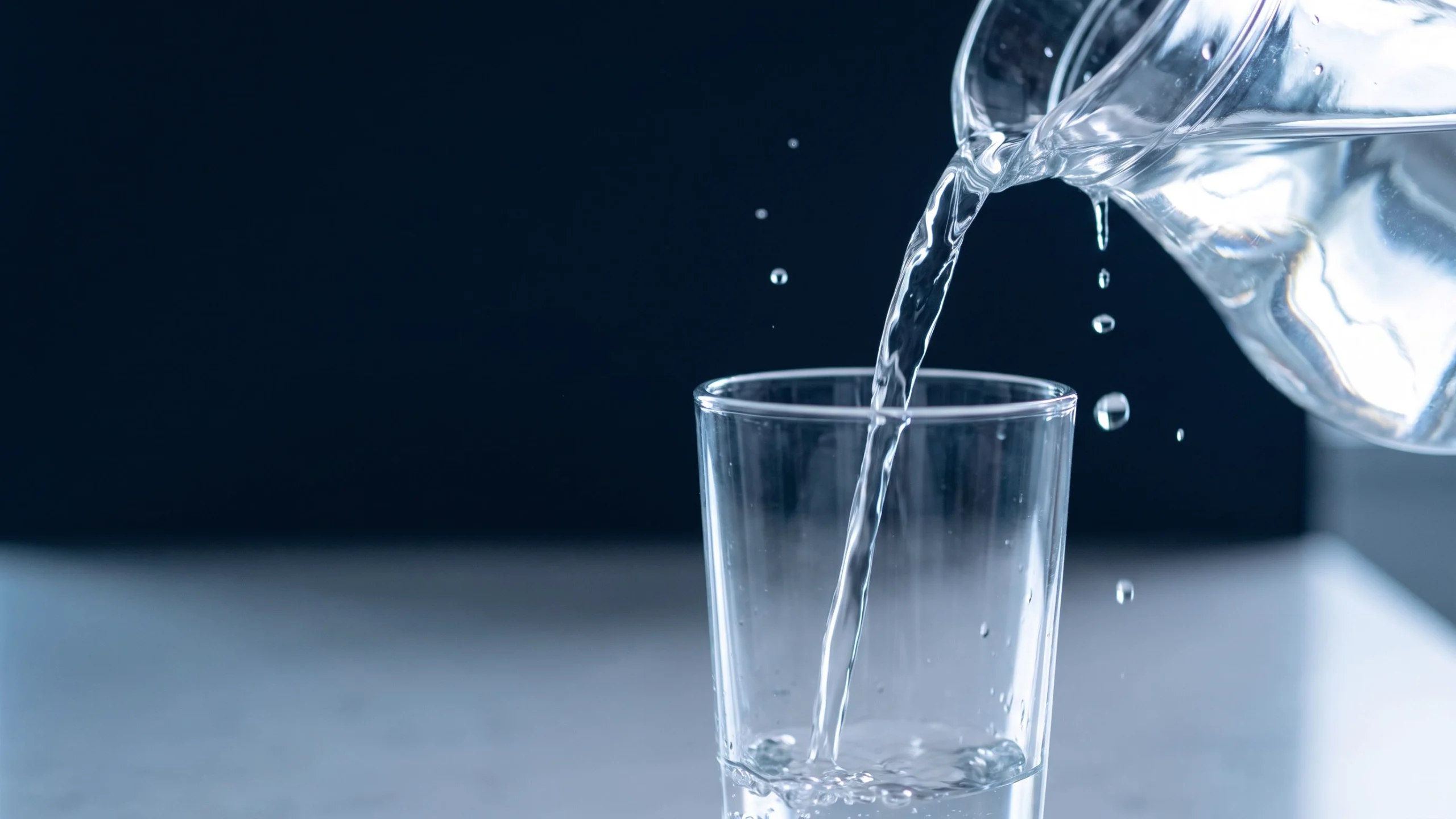 Still water being poured from a clear glass jug into a drinking glass