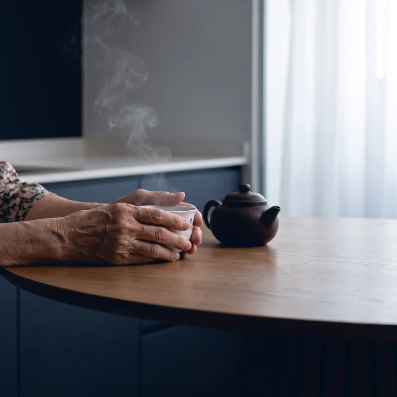 A grandmother's hands around a cup of tea at the kitchen table