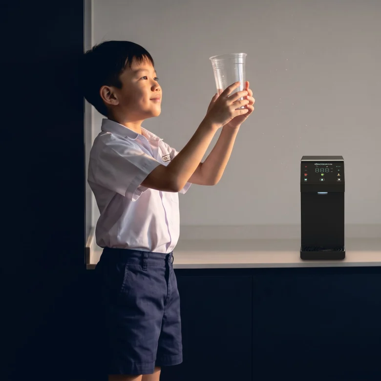 A boy in school uniform holding up an empty cup in the afternoon sun